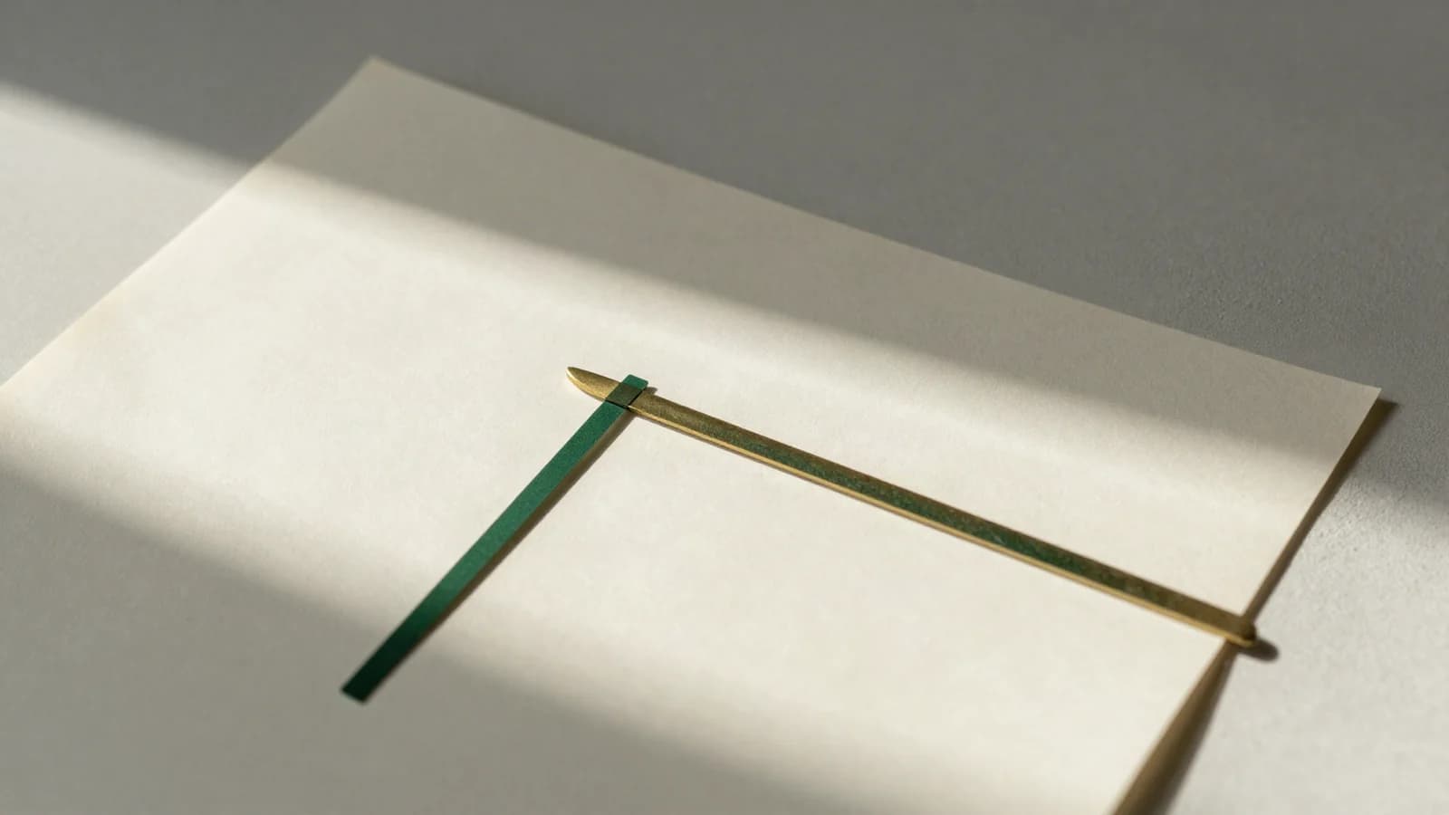 Morning light falling across a sheet of cream accounting paper, with a brass rule and a green rule laid across it.